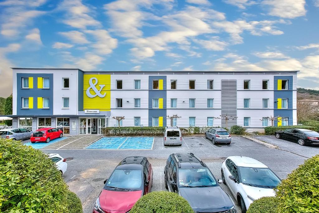 un grand bâtiment blanc avec des voitures garées dans un parking dans l'établissement B&B HOTEL Antibes Sophia Antipolis, à Biot