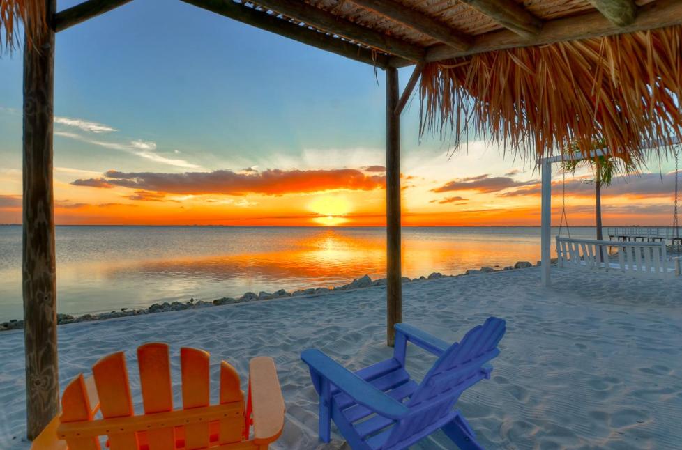 two chairs and a umbrella on a beach with the sunset at Casa de Playa - Waterfront with Amazing Sunset, Pool and WIFI in Tampa
