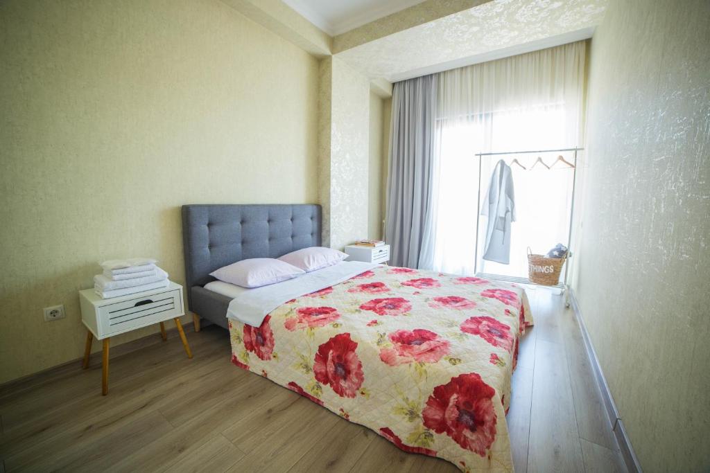 a bedroom with a bed with a floral bedspread and a window at Comfy Apartment in Tbilisi City