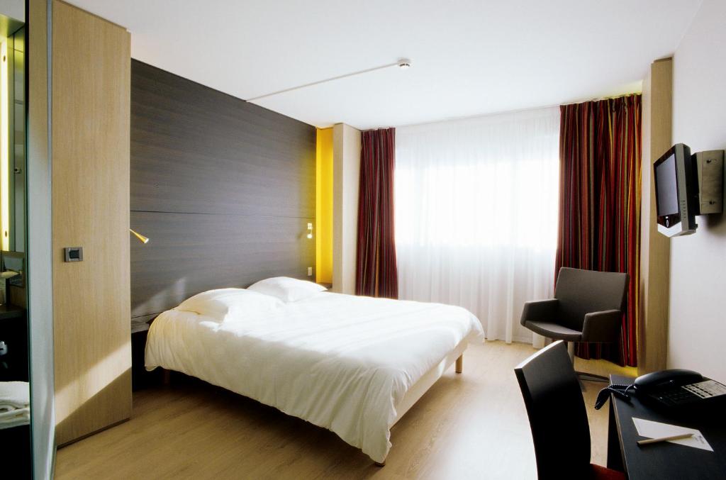 a hotel room with a white bed and a chair at Oceania Quimper in Quimper