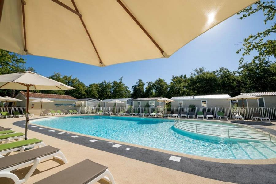 une grande piscine avec des chaises et un parasol dans l'établissement Camping Les Chèvrefeuilles - Maeva, à Royan