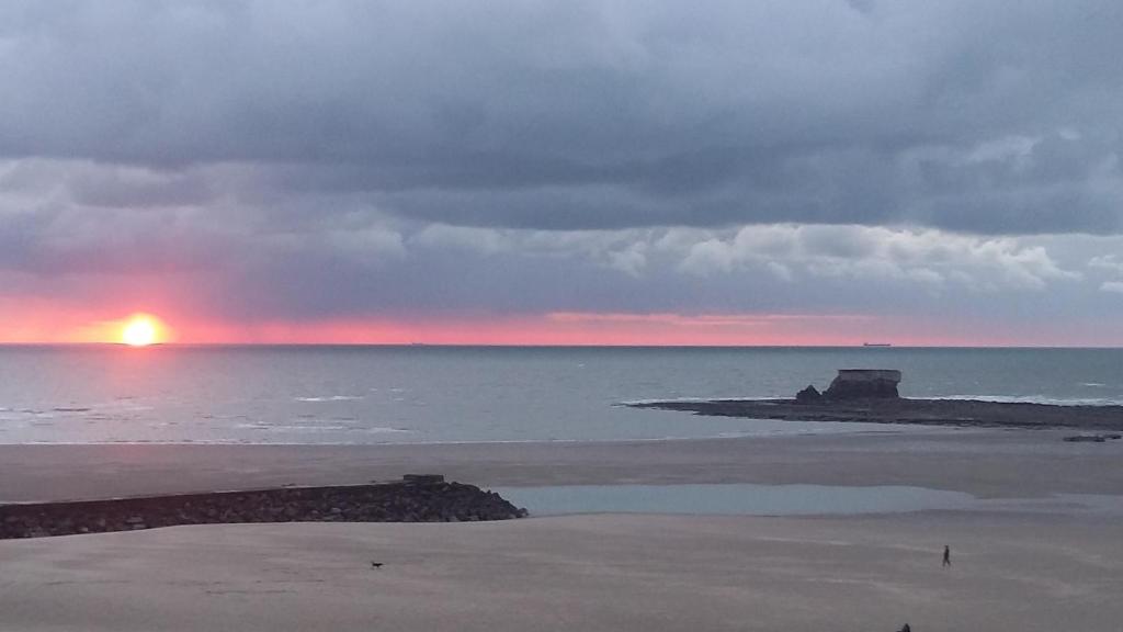 una puesta de sol sobre el océano con una playa y el horizonte en Appt face mer, en Le Portel
