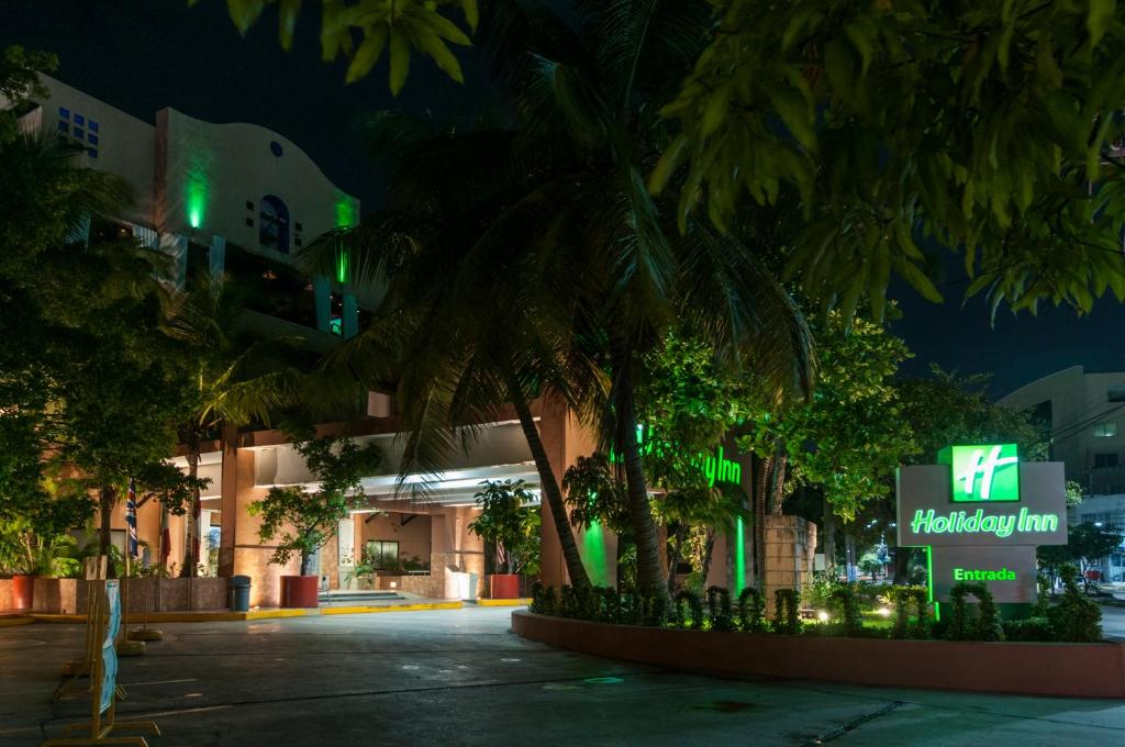 een gebouw met palmbomen er 's nachts voor bij Holiday Inn Ciudad Del Carmen, an IHG Hotel in Ciudad del Carmen