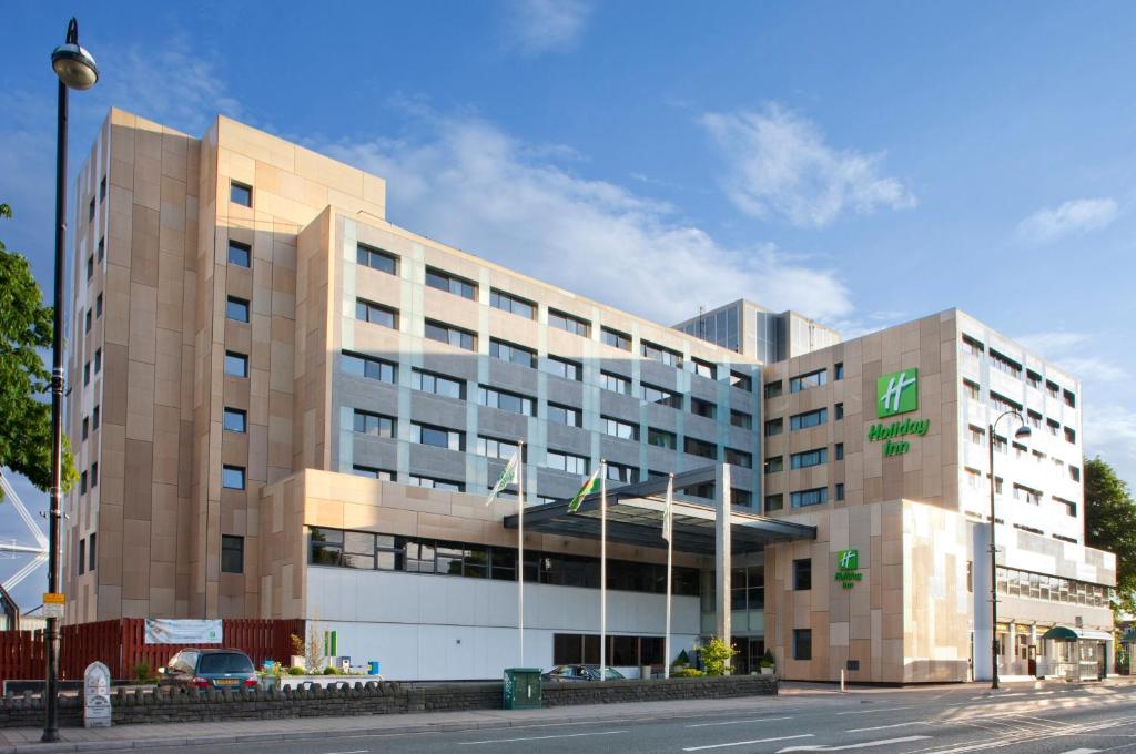 un grande edificio con un'auto parcheggiata di fronte di Holiday Inn Cardiff City, an IHG Hotel a Cardiff