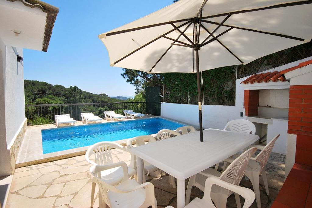 un tavolo bianco con sedie e ombrellone accanto alla piscina di Club Villamar - Caramel a Lloret de Mar