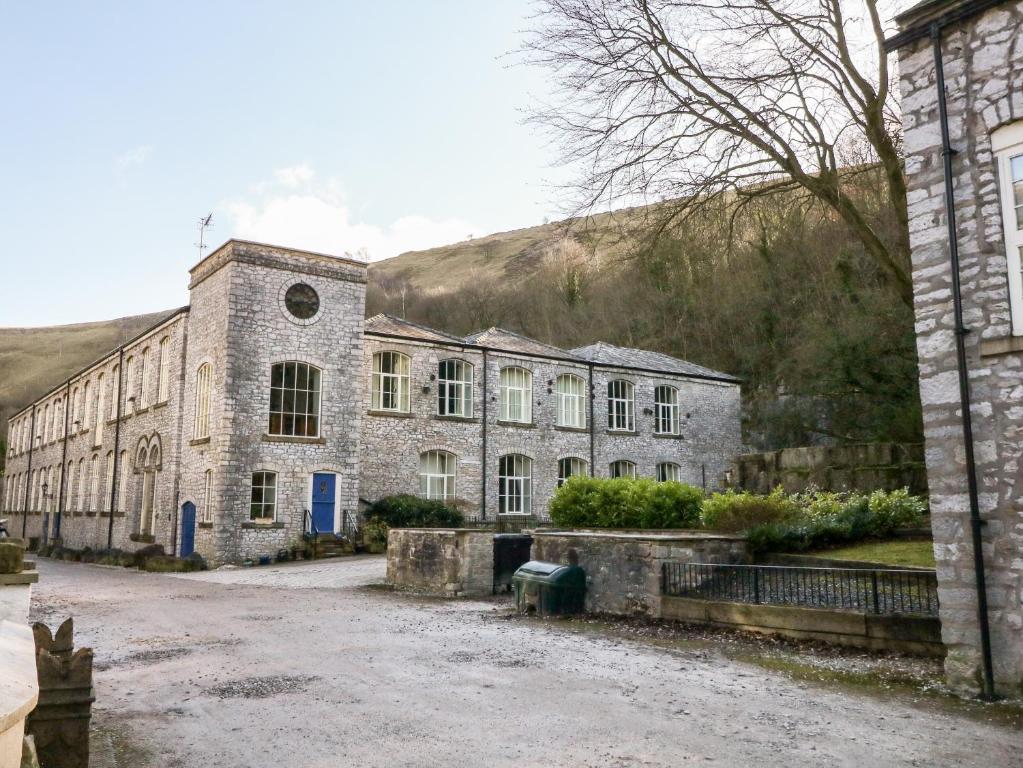an old stone building with a hill in the background at Wye Apartment, Litton Mill in Buxton