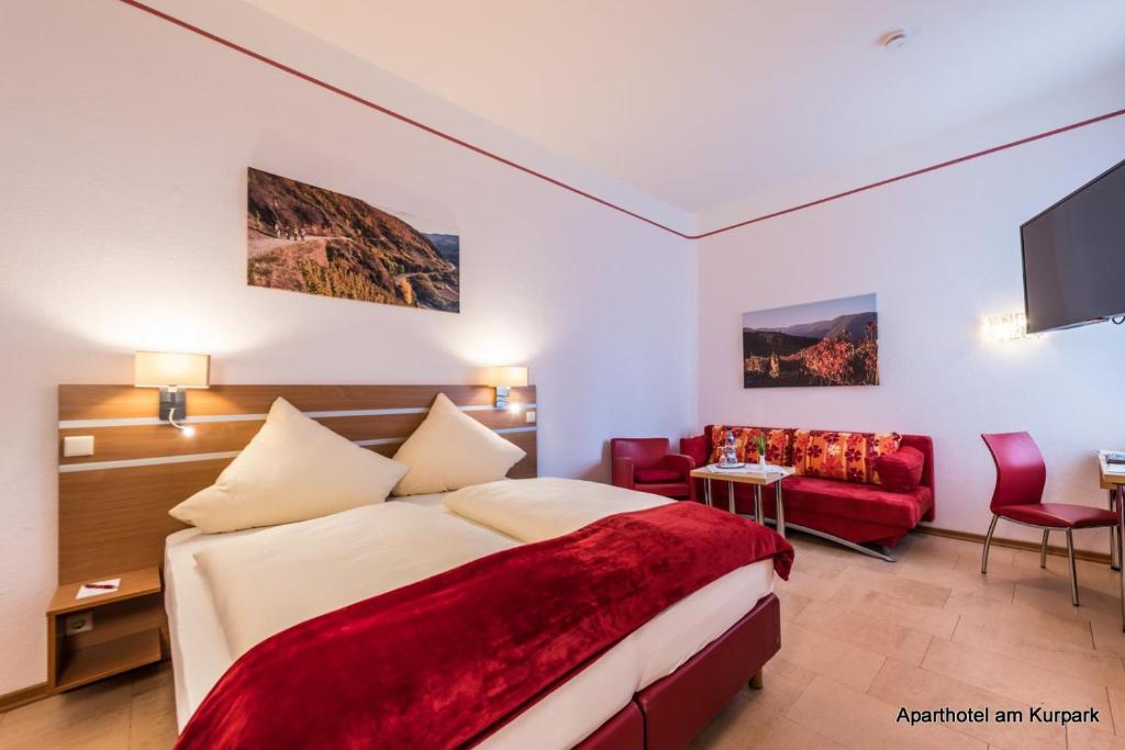 バート・ノイェンアール・アールヴァイラーにあるAparthotel am Kurparkのベッドと赤いソファが備わるホテルルームです。