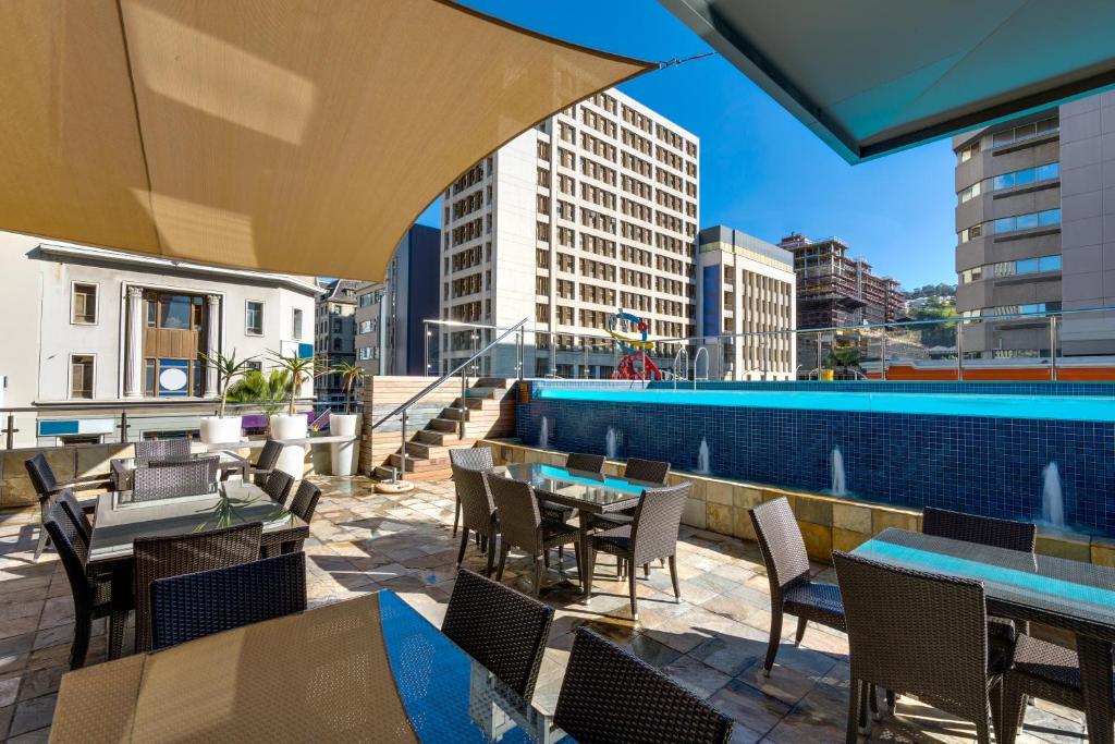 een terras met tafels en stoelen en een zwembad bij Cresta Grande Cape Town in Kaapstad