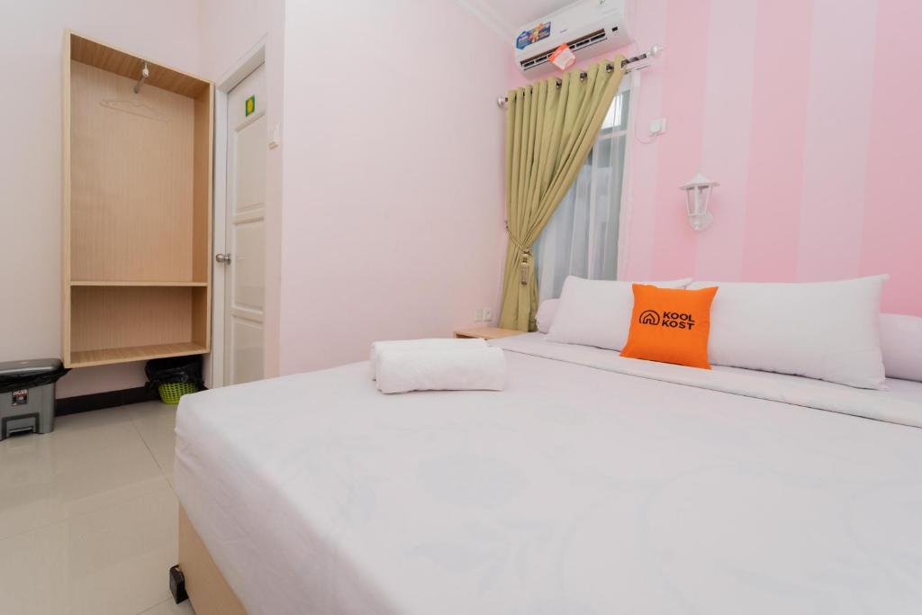 - une chambre avec un grand lit blanc et un oreiller orange dans l'établissement KoolKost Syariah near Taman Bekapai Balikpapan, à Klandasan Kecil