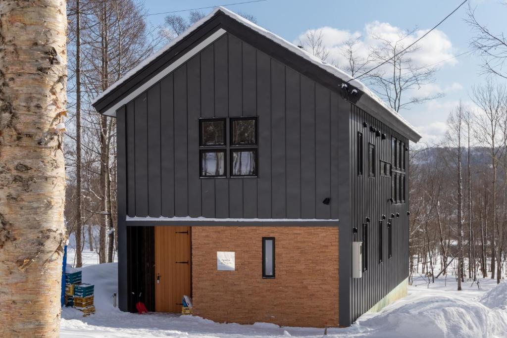 ein schwarzes Haus mit brauner Tür im Schnee in der Unterkunft Iguru Ski Chalet - walking distance to Rusutsu Resort in Rusutsu
