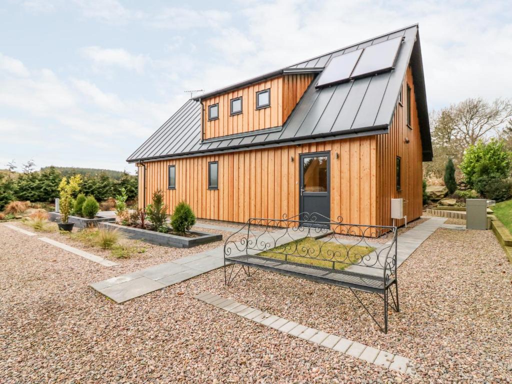 una casa de madera con techo negro y banco en Larchwood Lodge en Ellon