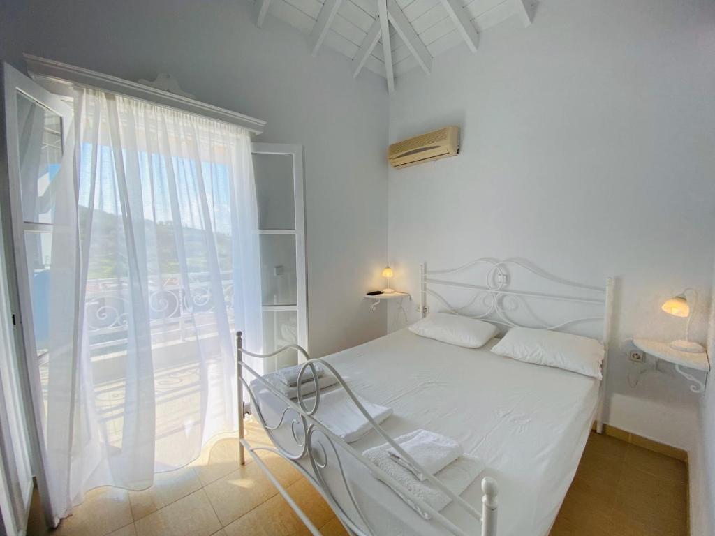 a white bedroom with a bed and a large window at Pontamos Villas in Halki