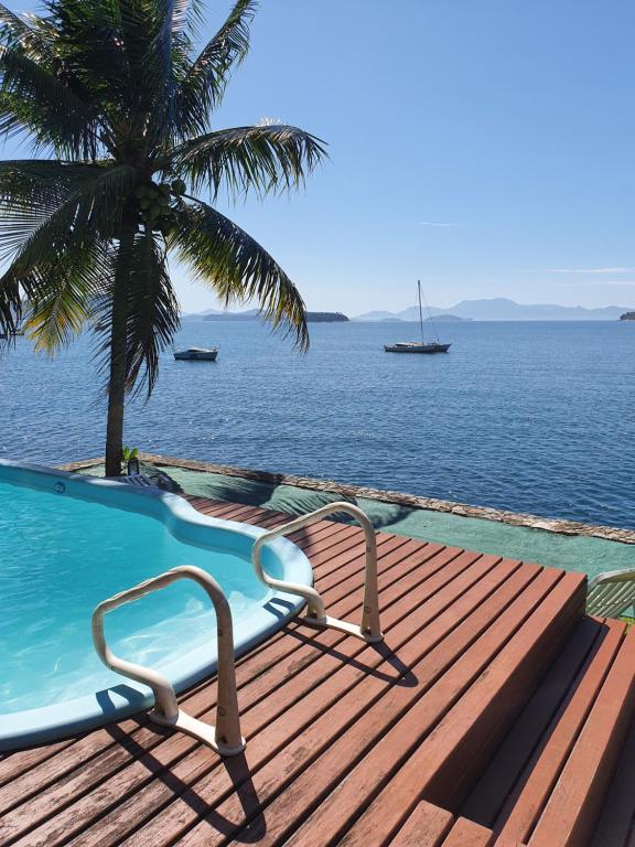 a swimming pool with a palm tree and the ocean at Ocean Green Flats in Angra dos Reis