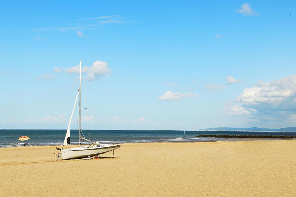 a sailboat sitting on a beach with the ocean at Beautiful Beach Front Cottage in Llandudno