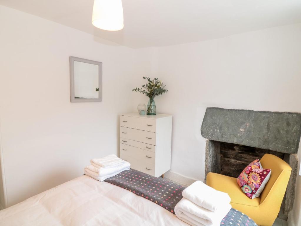 a bedroom with a fireplace and a yellow chair at 1 Jubilee Cottage in Tintagel