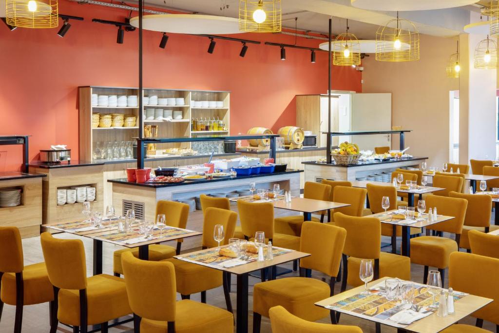 a restaurant with tables and yellow chairs and a kitchen at SOWELL RESIDENCES Chênes Verts in Saint-Raphaël
