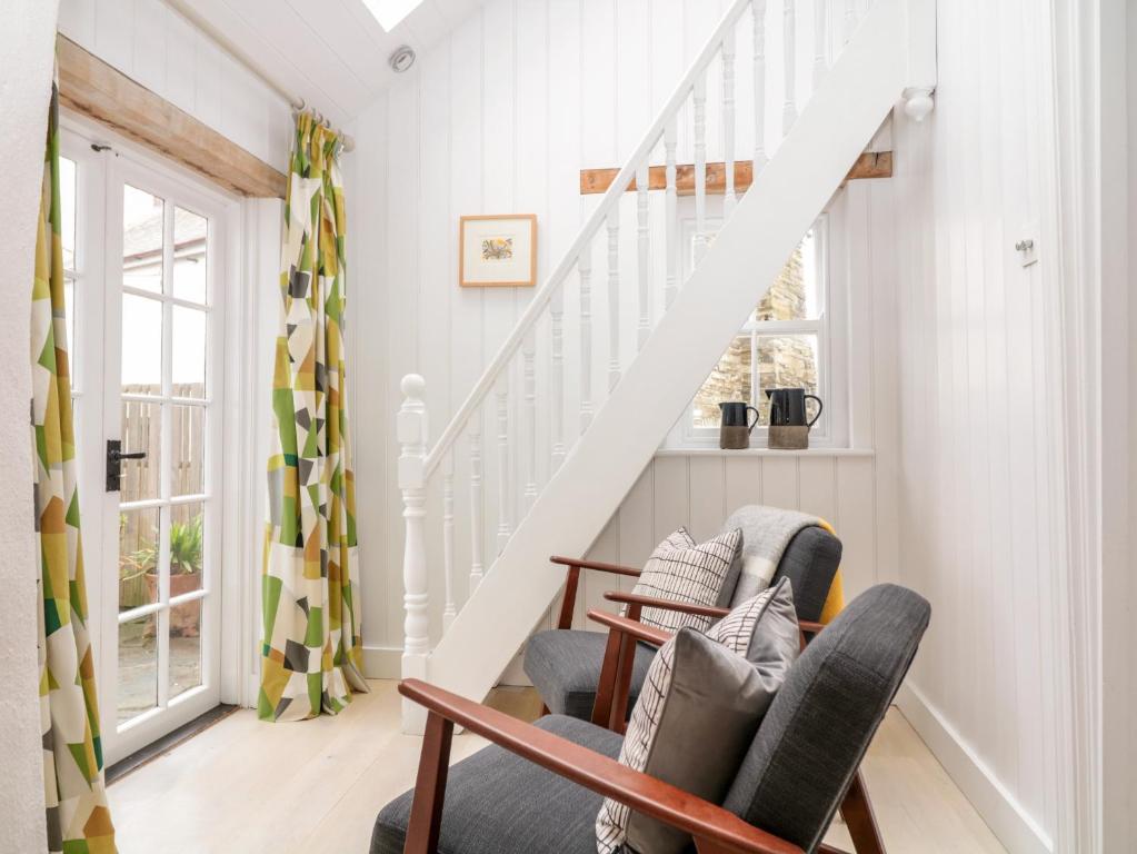 a living room with a staircase and two chairs at 1 Jubilee Cottage in Tintagel