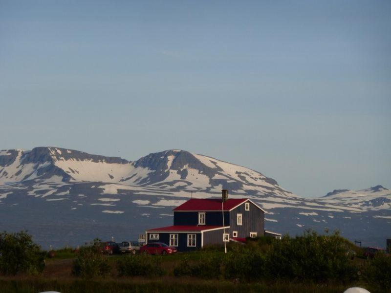 ein Haus mit rotem Dach vor schneebedeckten Bergen in der Unterkunft Húsey Hostel & Horsefarm in Egilsstaðir