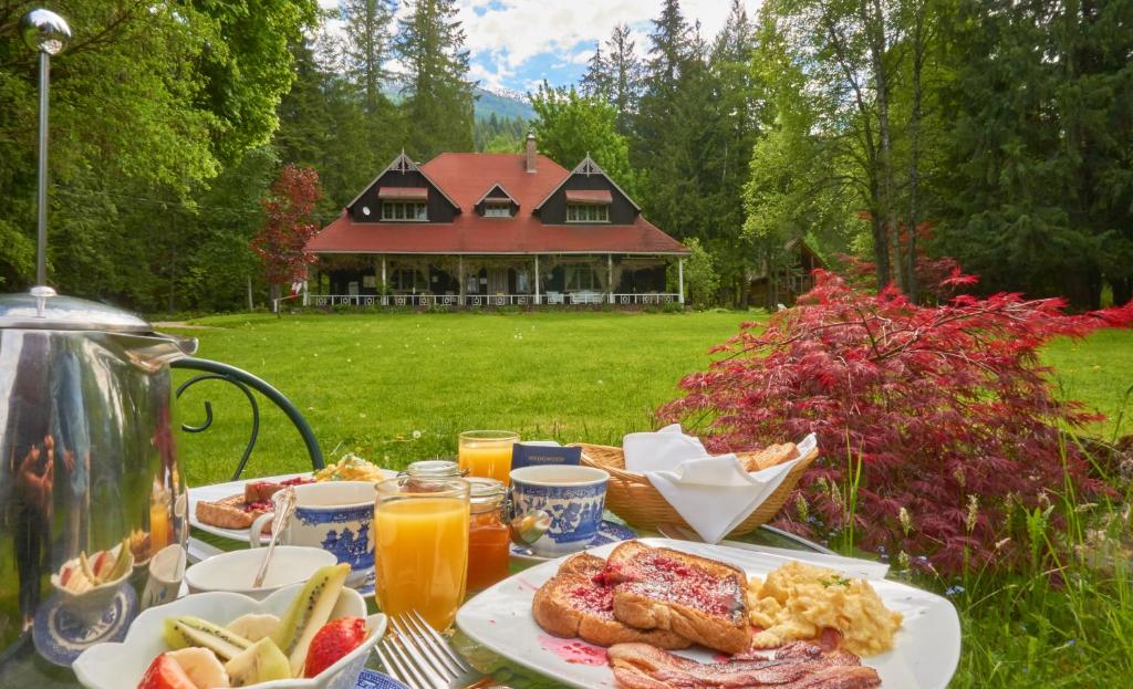 a table with breakfast food and a house in the background at Wedgwood Manor and Glamping Retreat in Crawford Bay