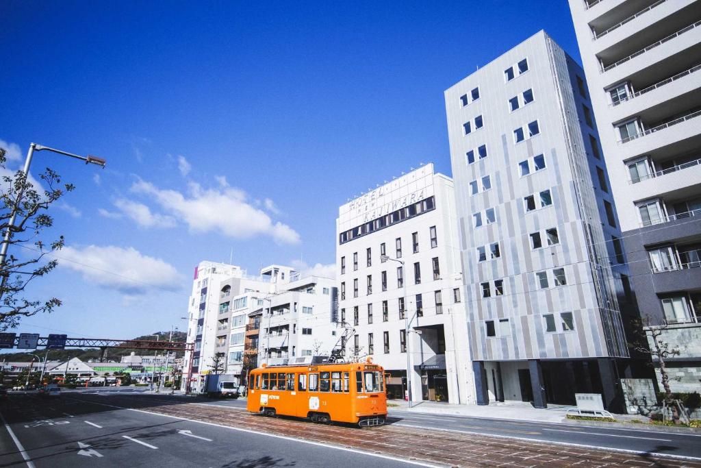 un autobús naranja estacionado en una calle de la ciudad con edificios en Hotel Kajiwara en Matsuyama