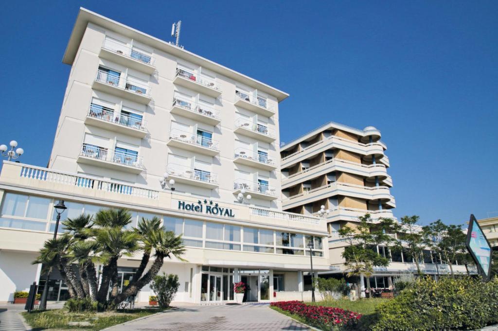 un grand bâtiment blanc avec des palmiers devant lui dans l'établissement Hotel Royal, à Cesenatico