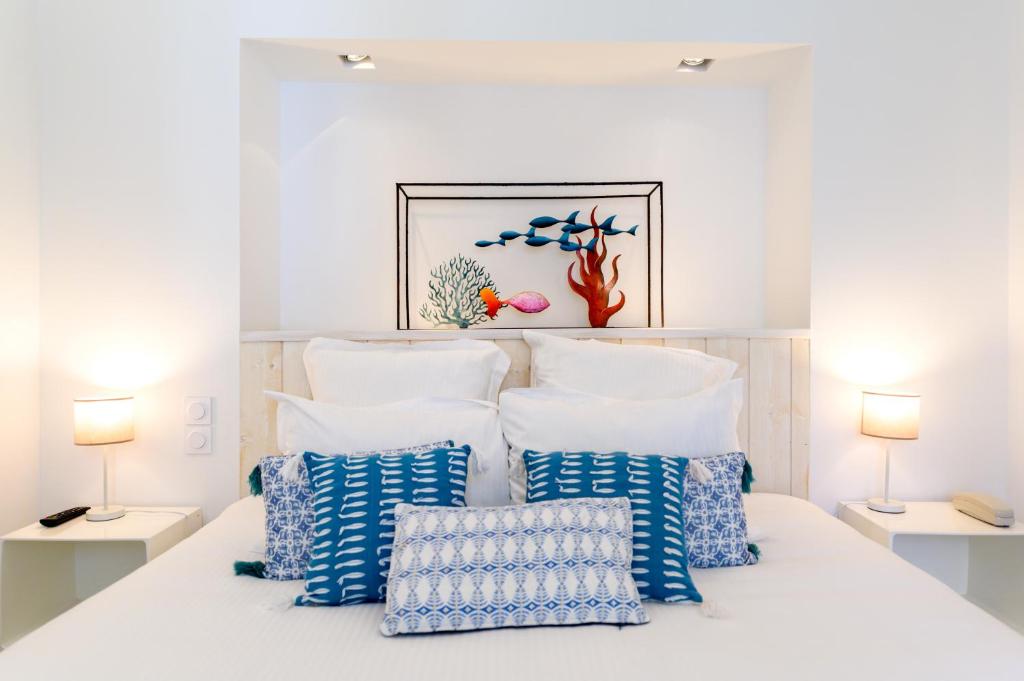a white bedroom with blue and white pillows on a bed at Hôtel La Jetée in Saint-Martin-de-Ré