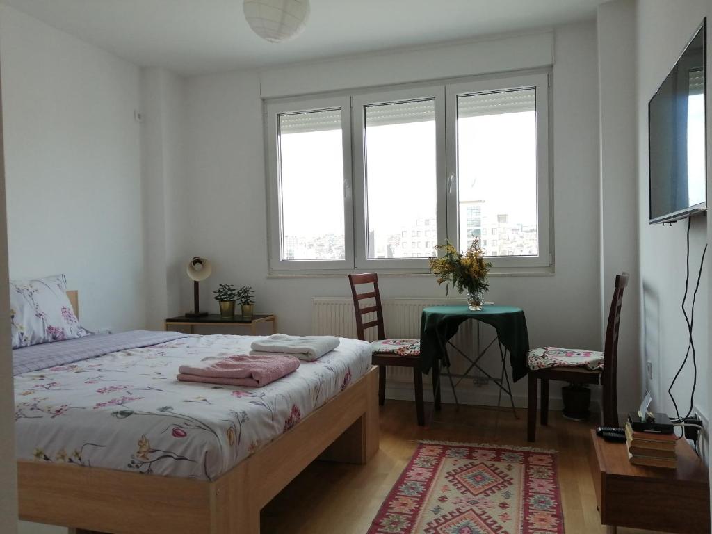 um quarto com uma cama, uma mesa e janelas em Super Central & Panoramic Nick's Apartment em Pristina