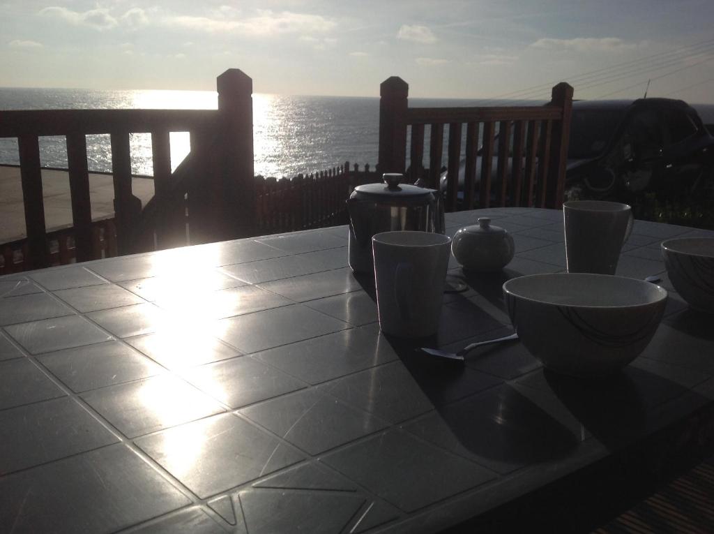a table with bowls and cups on a balcony with the ocean at Sunset Ridge in Ventnor