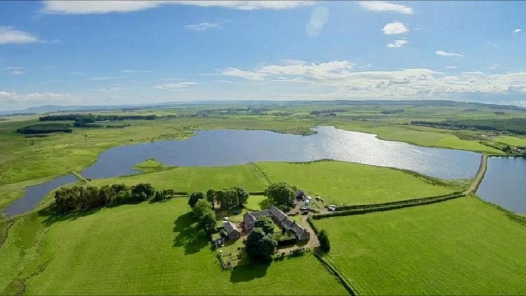 an aerial view of a house on a field next to a lake at Charming cottage with loch and hill views nr Edinburgh in Cobbinshaw