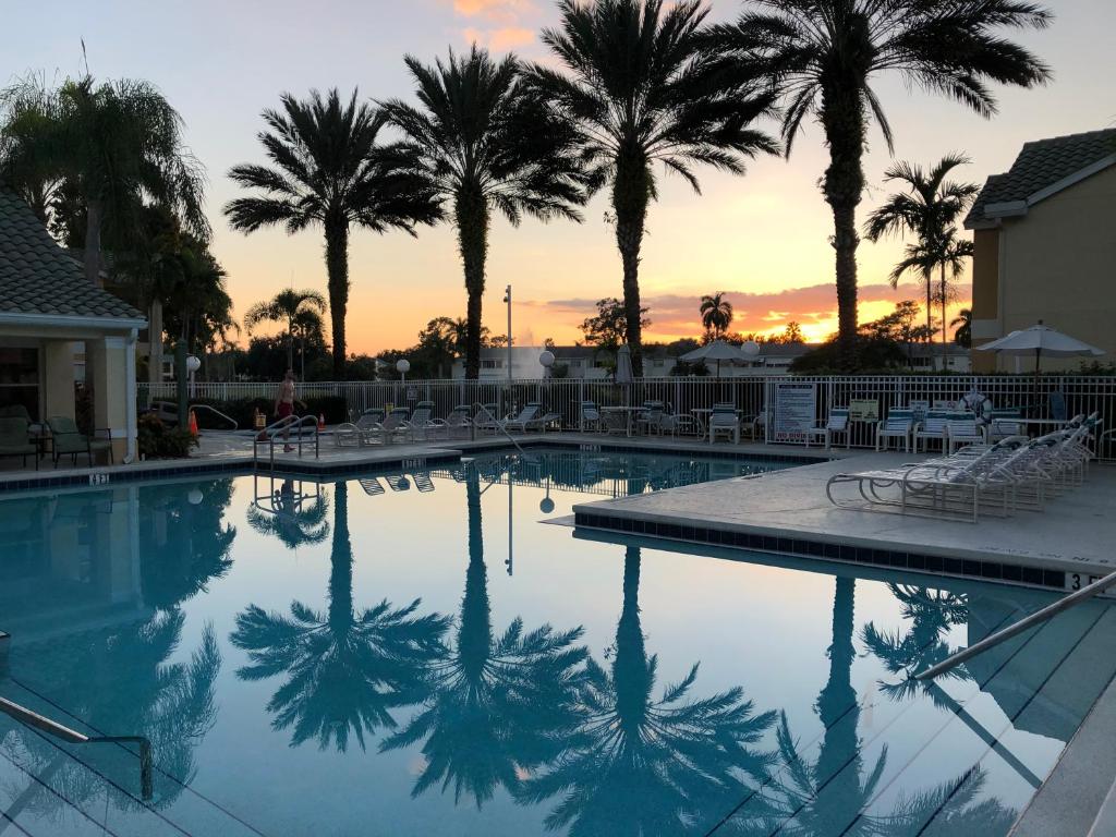 a pool with palm trees and chairs and a sunset at Beautiful two master bedroom condo in Fort Myers, Venetian Palms condominium in Fort Myers