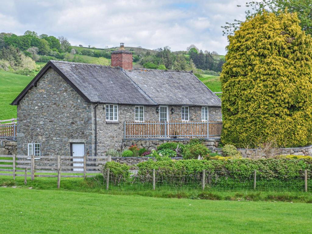 an old stone house with a fence in a field at Hafan in Llanerfyl