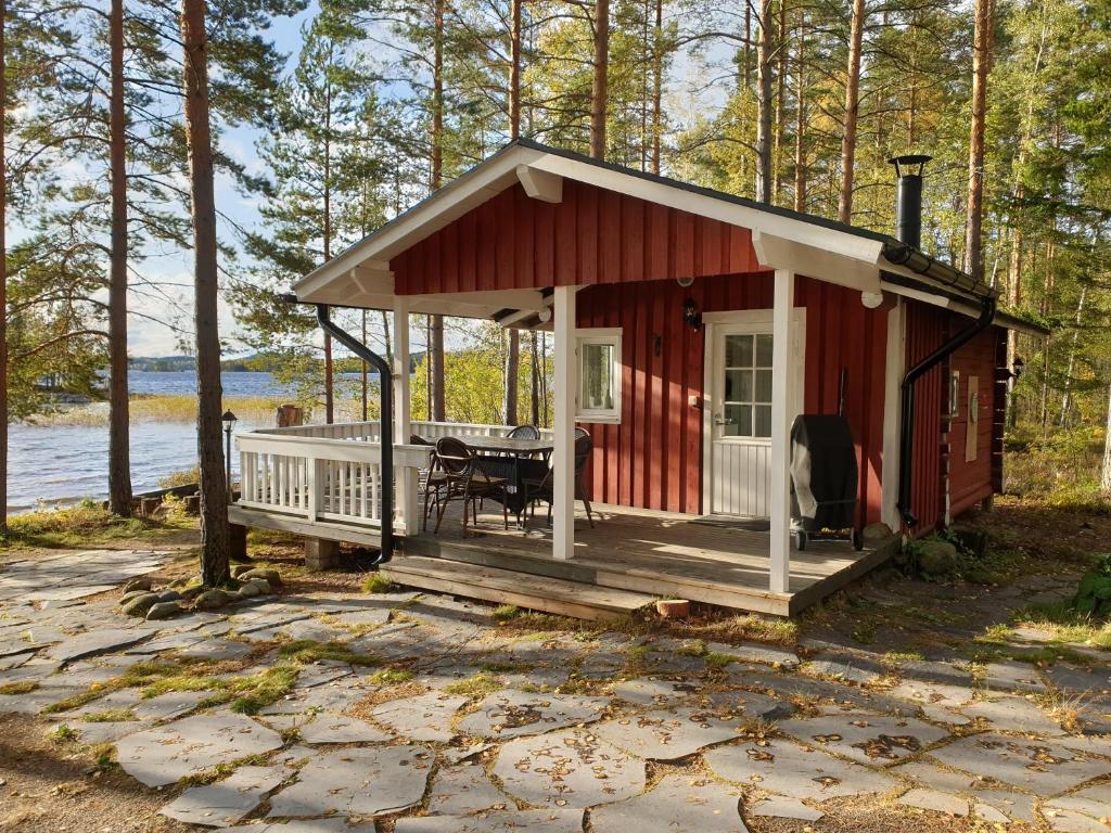 a small red cabin with a porch and a table at Nestorin maja in Puumala