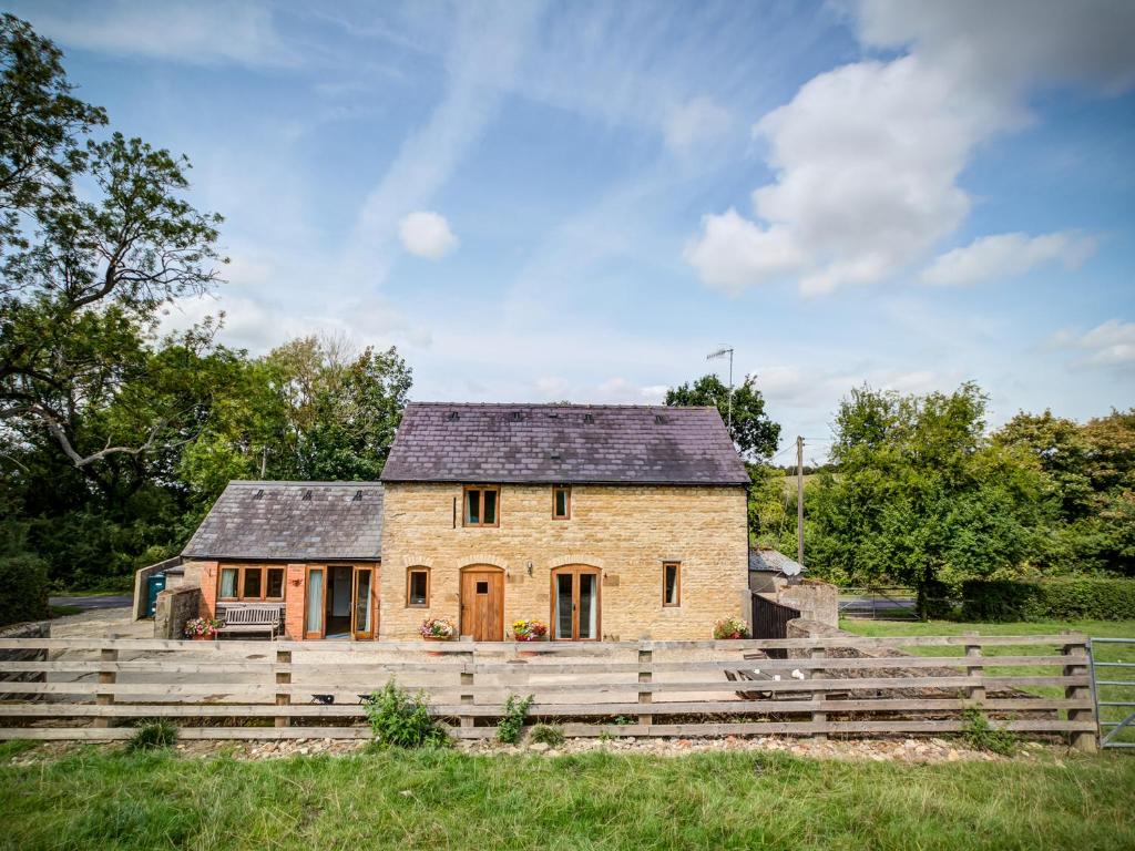 a stone house in a field with a wooden fence at Little Barn in Cherington