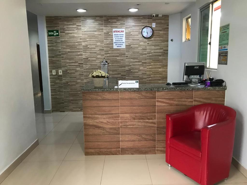 a red chair in a waiting room with a clock on a wall at Hotel Oliveira in Goiânia