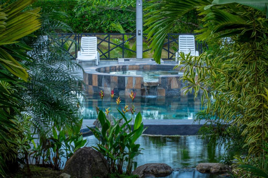 a swimming pool in a garden with two lawn chairs at Residencias Arenal in Fortuna