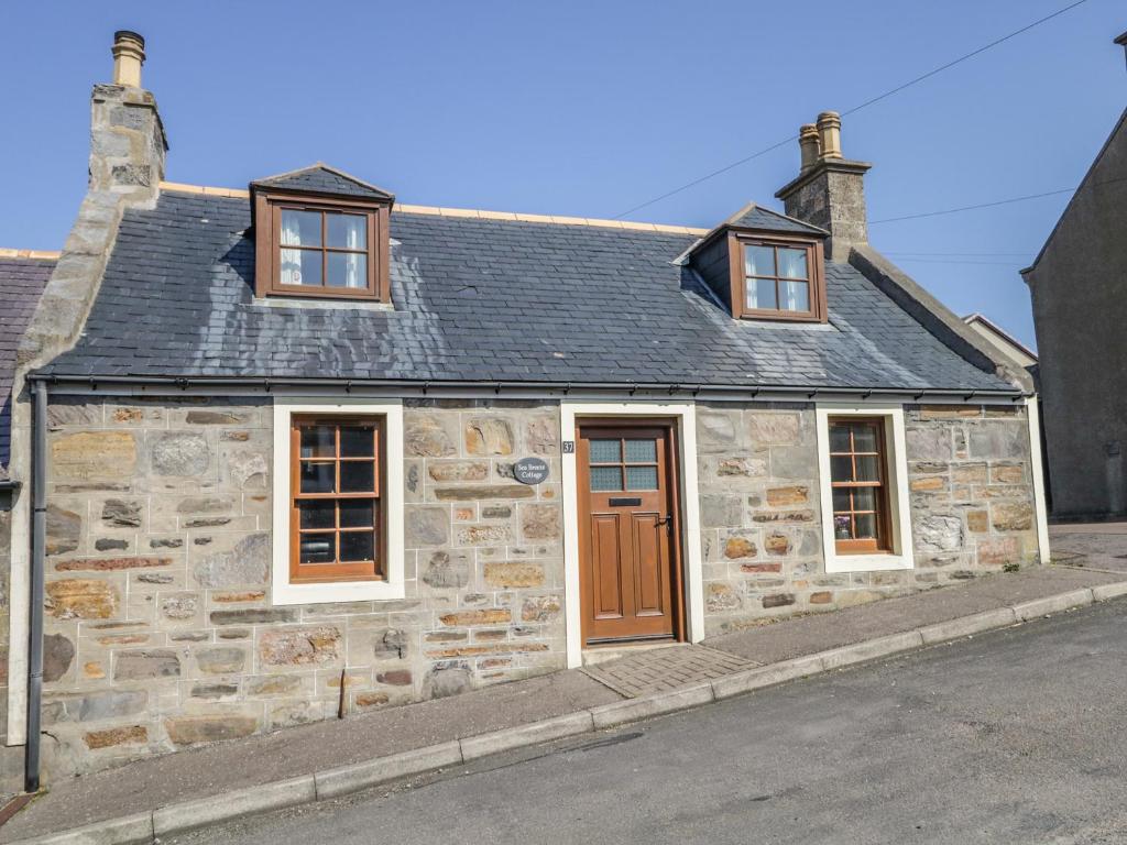 an old stone house with three windows on a street at Sea Breeze Cottage in Buckie