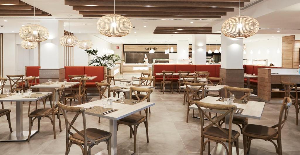 a dining room with tables and chairs and chandeliers at Insotel Club Tarida Playa in Cala Tarida