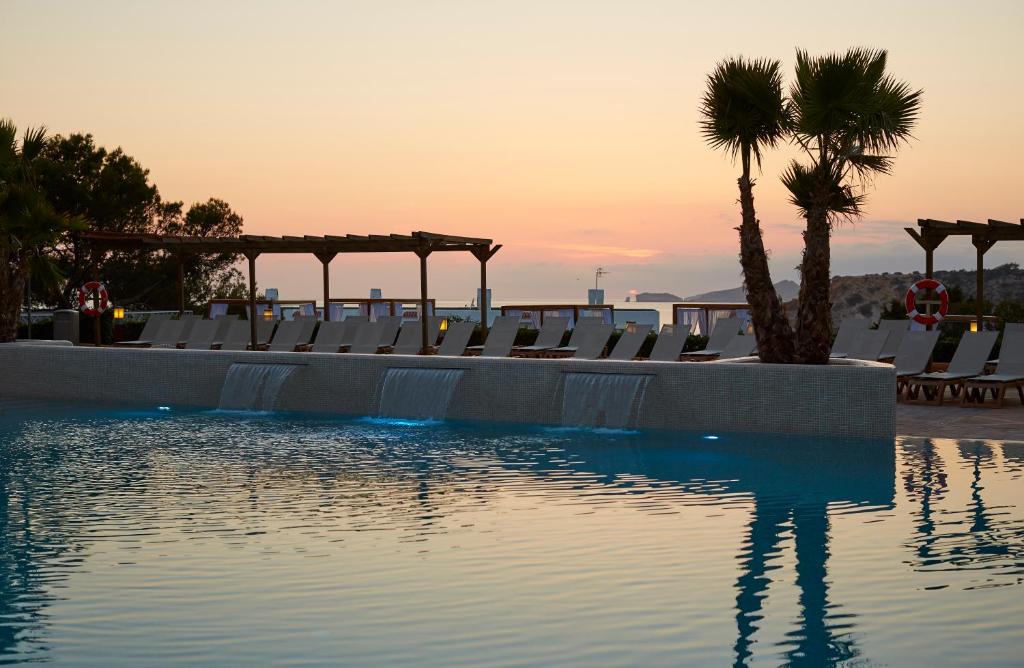 a pool with chairs and a palm tree and the sunset at Insotel Club Tarida Playa in Cala Tarida