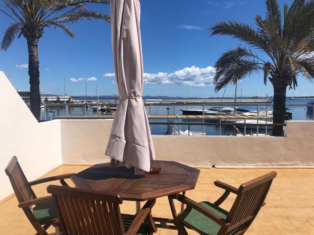 een houten tafel en stoelen met een parasol op een patio bij Apartamentos Mar i Vent Puerto de La Savina Formentera in La Savina