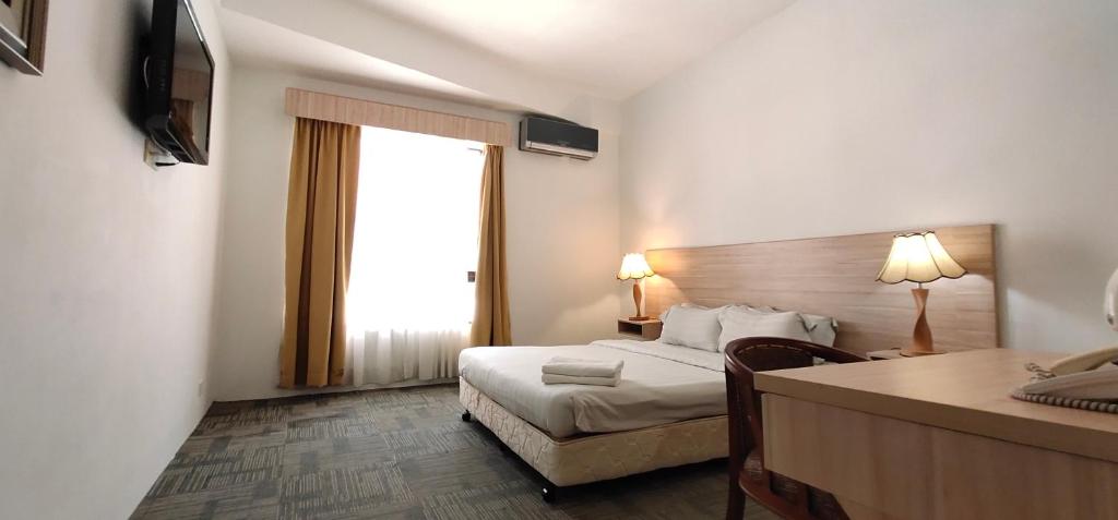 a hotel room with a bed and a desk and a window at Prima Hotel Melaka in Malacca