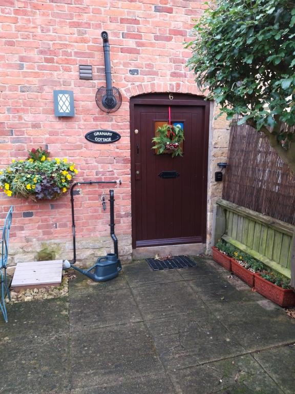 una puerta marrón con una corona junto a un edificio de ladrillo en Granary Cottage, en Mickleton