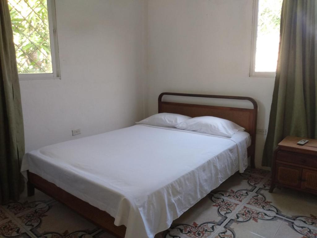 1 dormitorio con 1 cama con sábanas blancas y 2 ventanas en Hostal Santa Clara, en San Antero