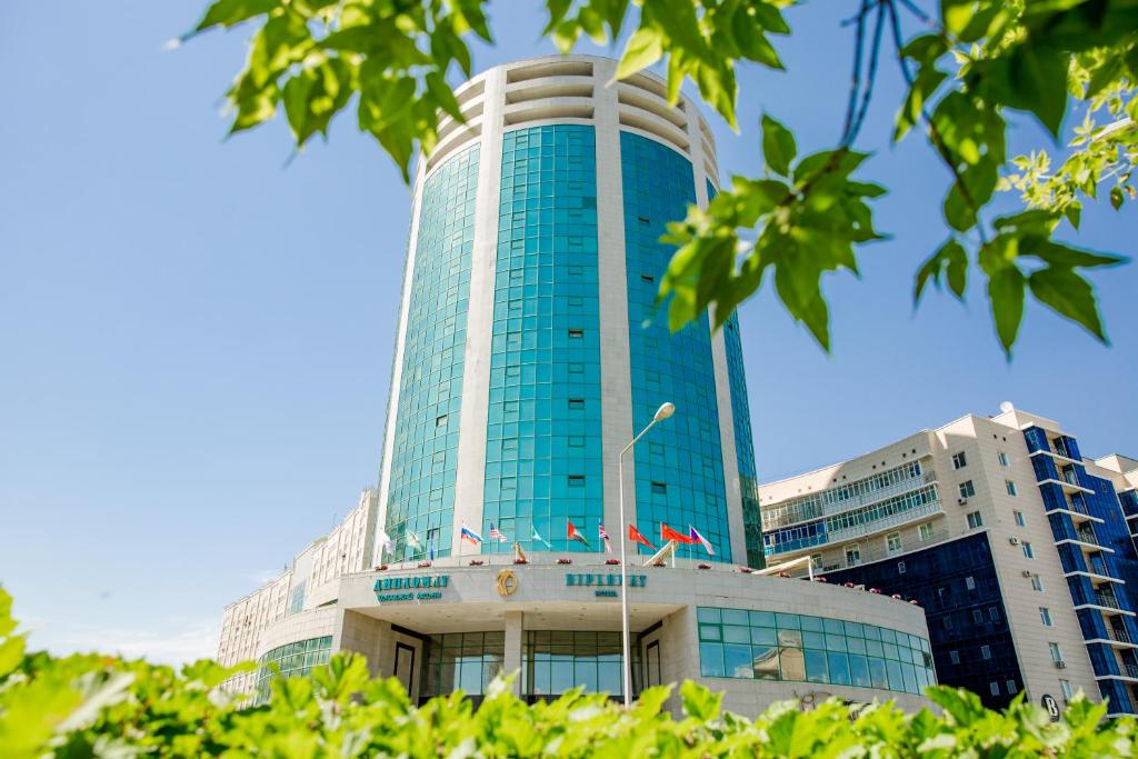 un grand bâtiment bleu avec des drapeaux devant lui dans l'établissement Diplomat Hotel by AG Hotels Group, à Astana