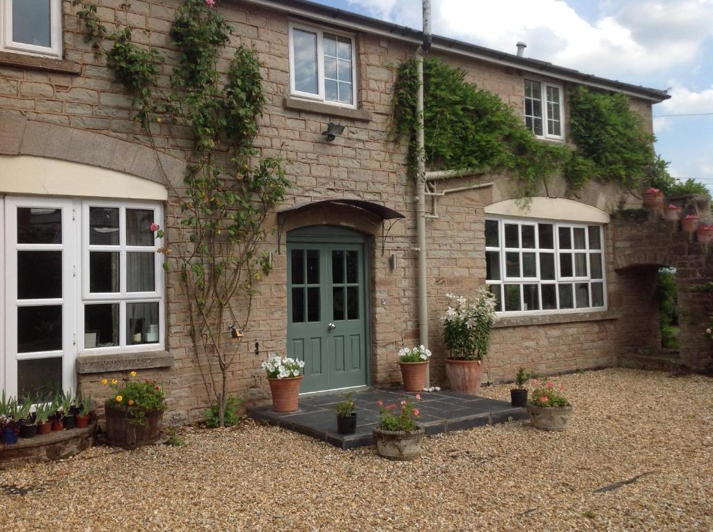 uma casa de tijolos com uma porta verde e alguns vasos de plantas em The Coach House em Ross on Wye