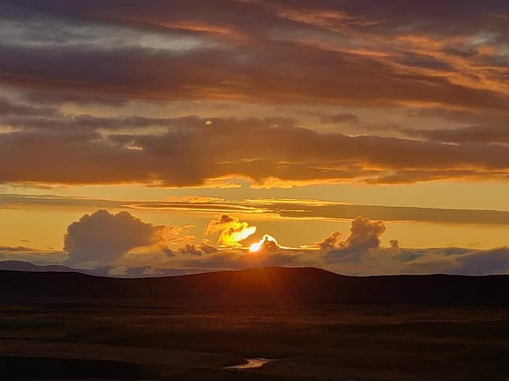 a sunset over a field with the sun in the clouds at Fjalladýrð Guesthouse in Modrudalur