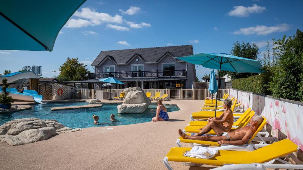 a group of people sitting on lounge chairs in a pool at Les Prairies de la Mer - Baie de Somme in Favières