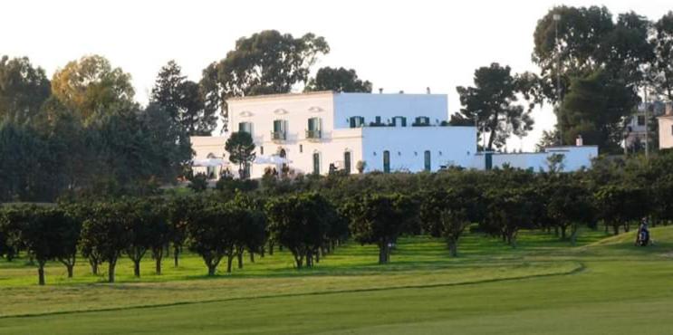 a white house behind a field of trees at Golf Club Metaponto in Metaponto