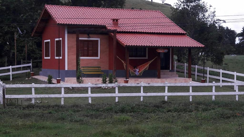 una casa roja con una valla blanca delante de ella en Encanto da Pedra en Visconde De Maua