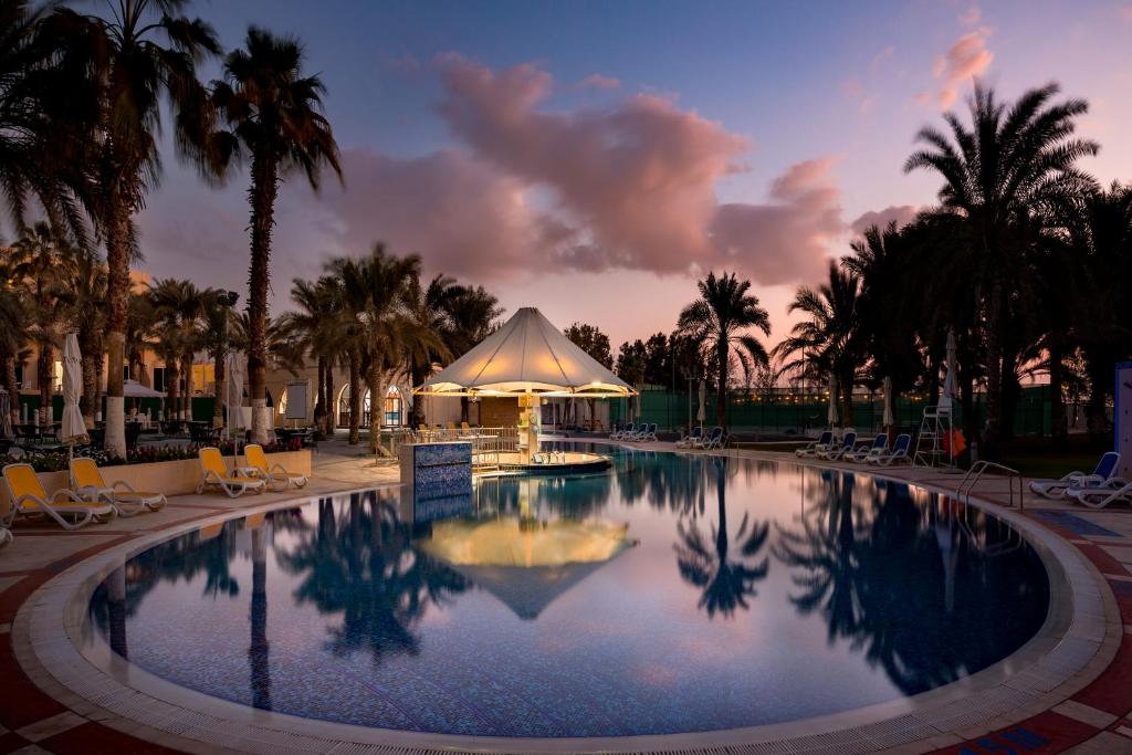 a large swimming pool with a tent and palm trees at Metropolitan Al Mafraq Hotel in Abu Dhabi