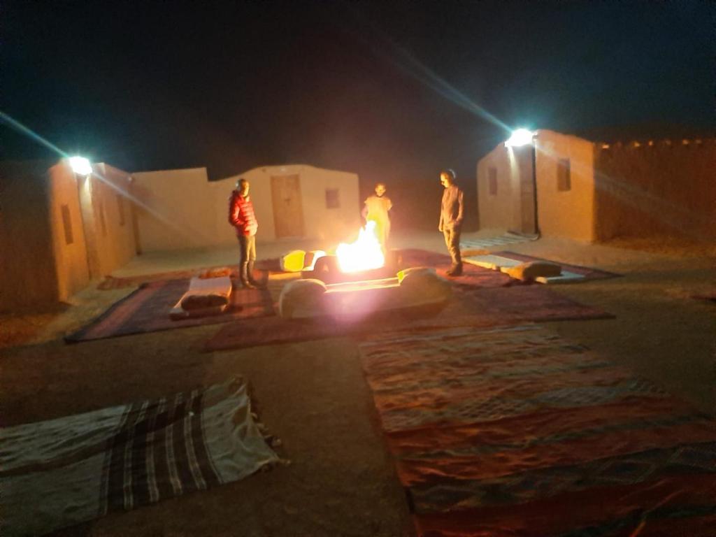 a group of people standing around a fire at night at Sahara Peace camp in Zagora